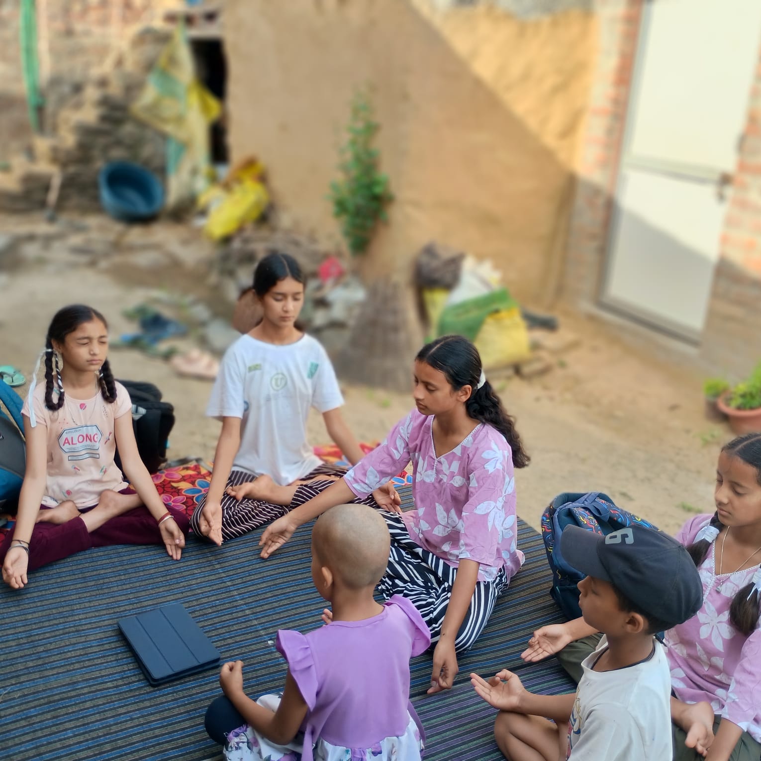 Children practicing mindful breathing around a tablet in a village courtyard