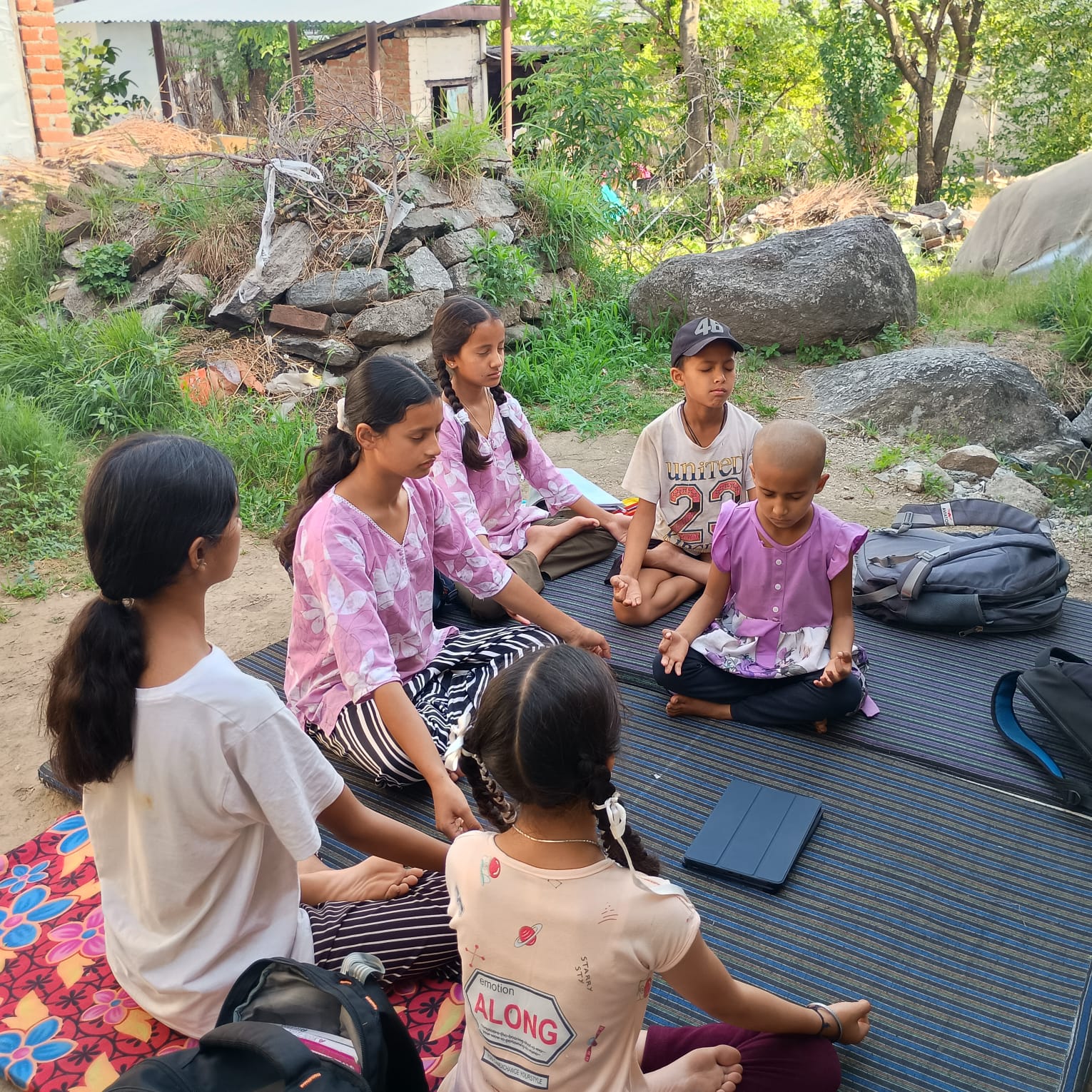 Children sitting in a mindful learning circle outdoors with a tablet nearby