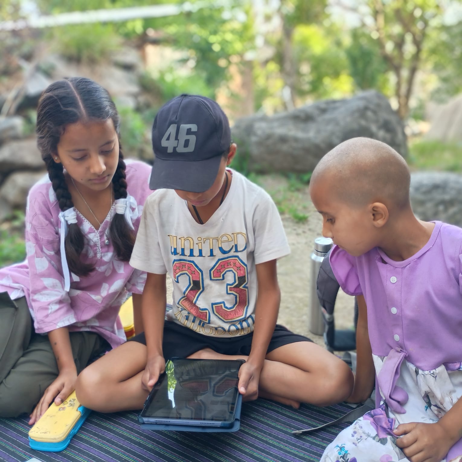 Three children looking closely at a tablet together during an outdoor lesson